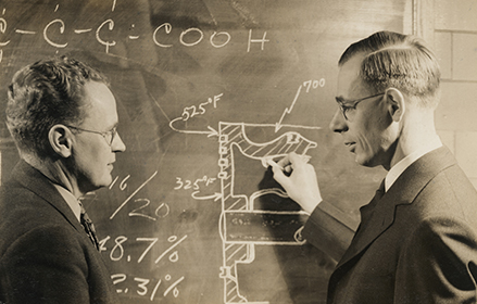 2 scientists writing in chalk on a chalk board