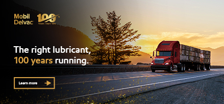 Golden light silhouettes a tall tree and rolling hills in the background, with the sky glowing orange. On the left, the Mobil Delvac logo and a “100 years since 1925” emblem appear. Large text reads, “The right lubricant, 100 years running.” The overall mood is rugged and celebratory, highlighting long‑haul reliability.